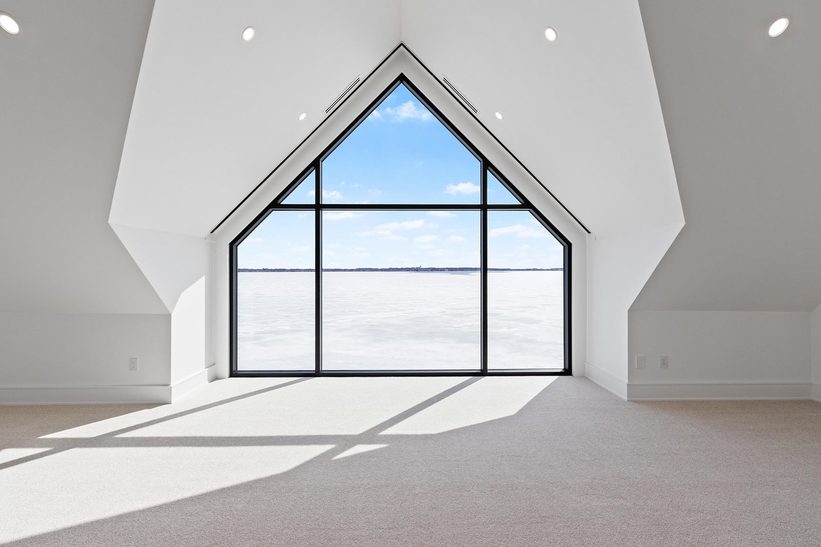 A-frame window looking out over a frozen lake from a bright upstairs loft