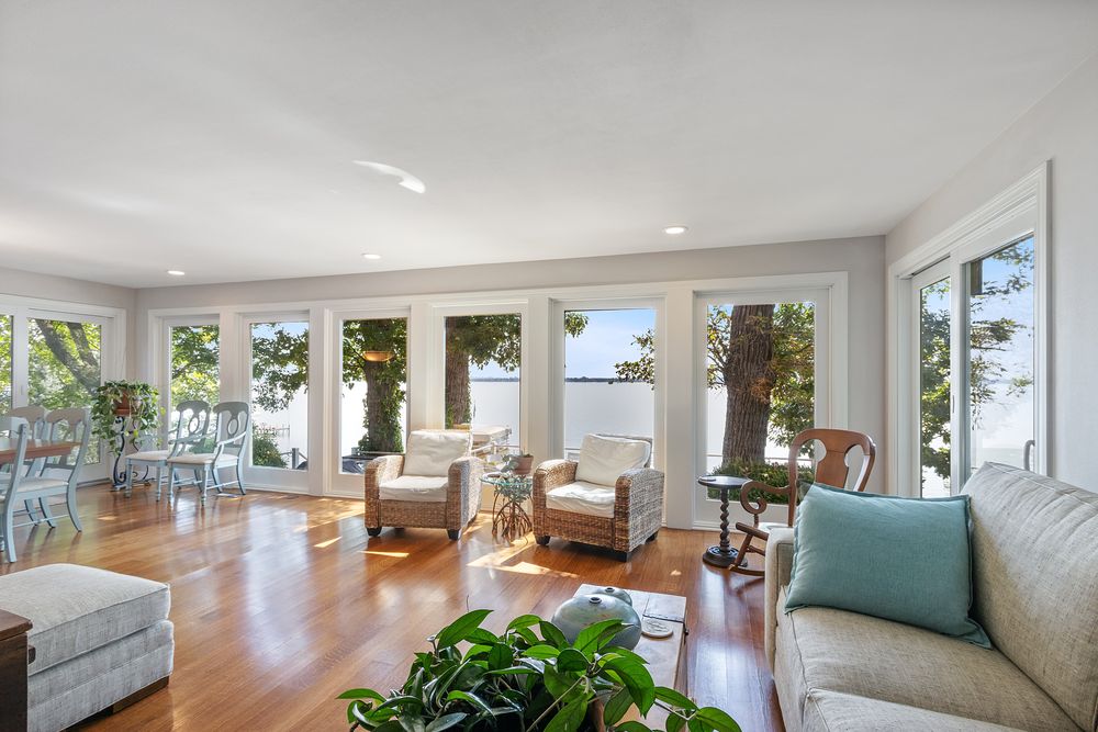Sunroom with wood floors and windows looking through trees to the lake
